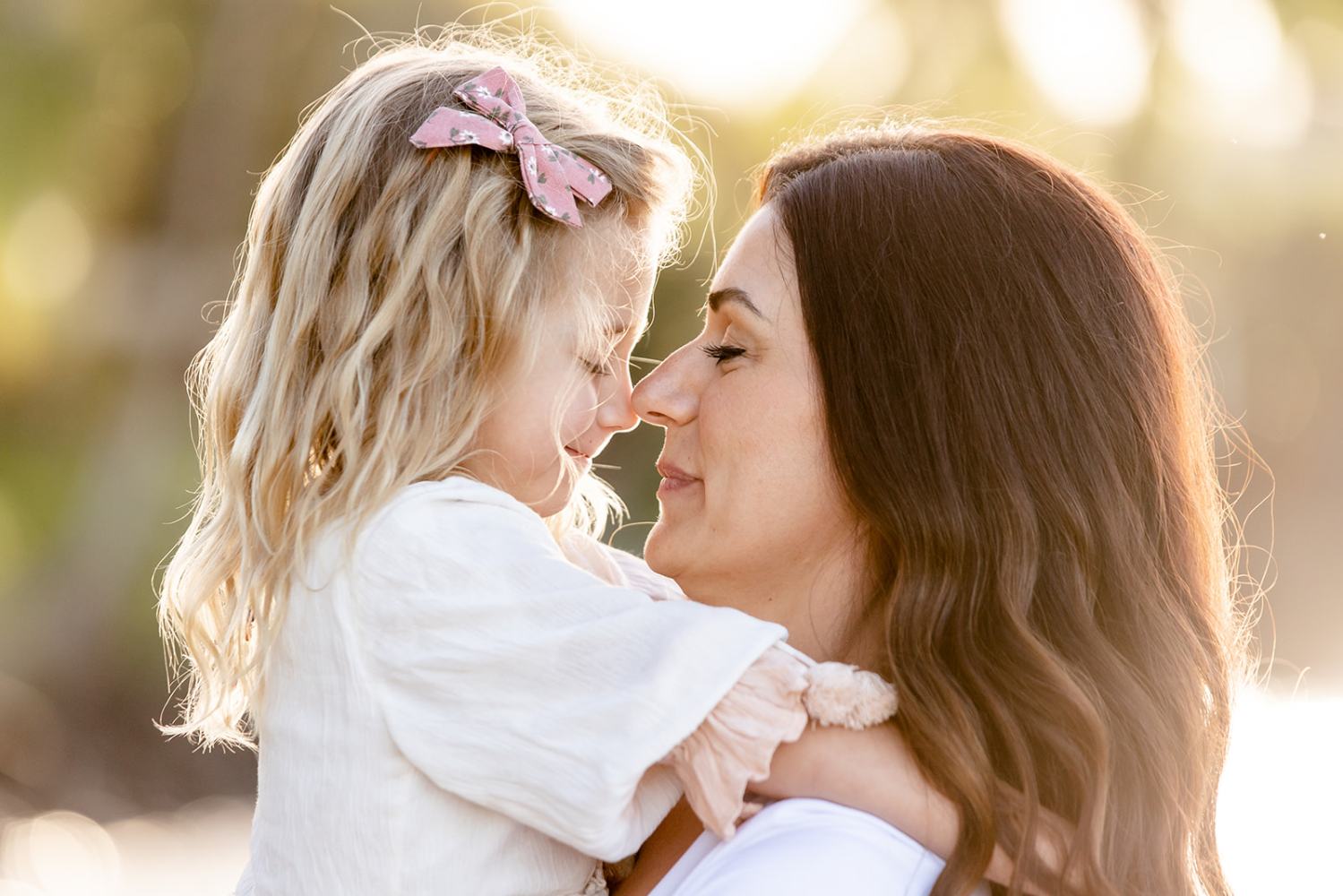 Woman and child touching noses, embracing in sunlight.