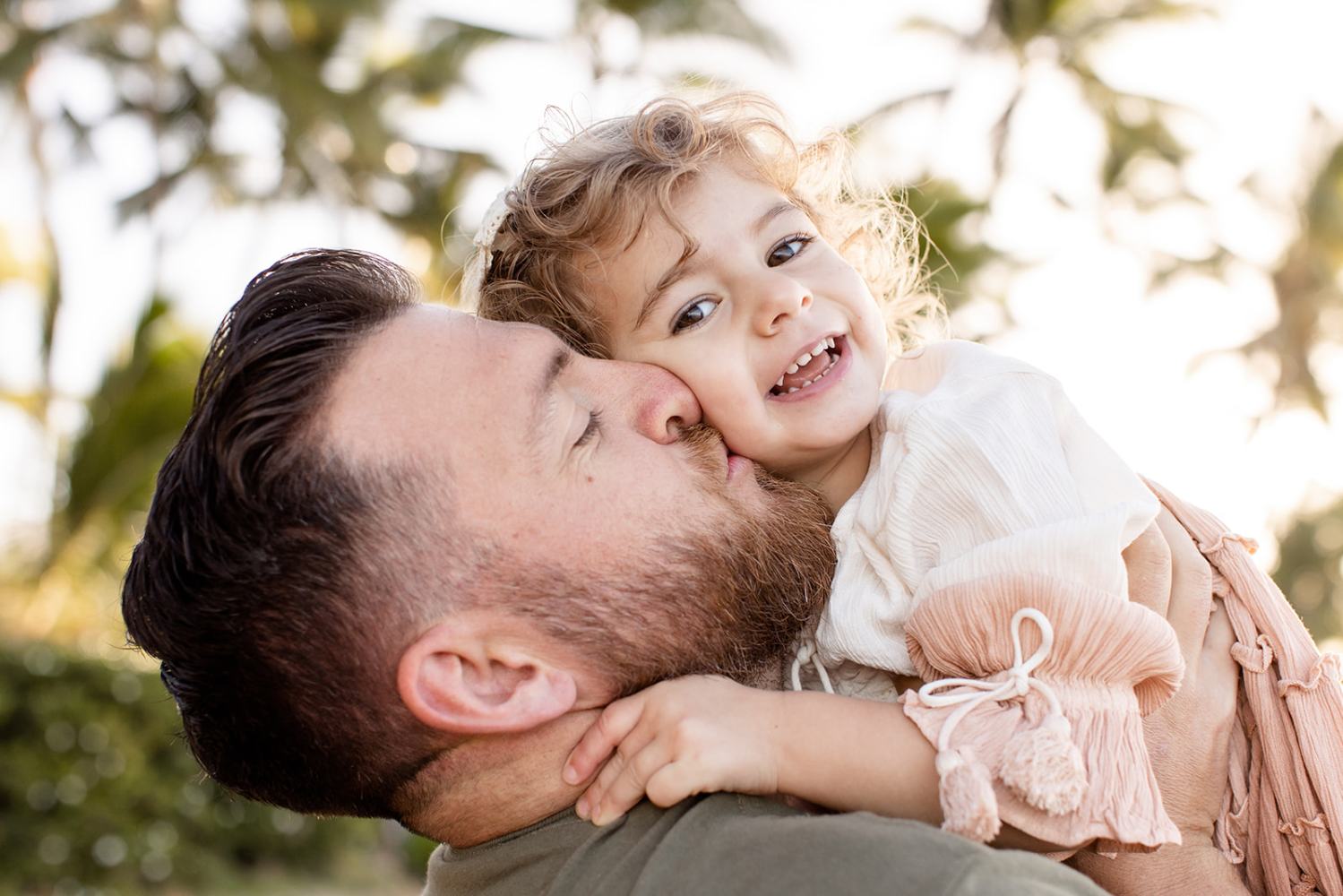 Man kissing smiling child held in arms, with trees in the background.