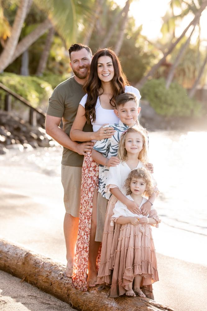 Smiling family of five standing on beach, with palm trees in background.