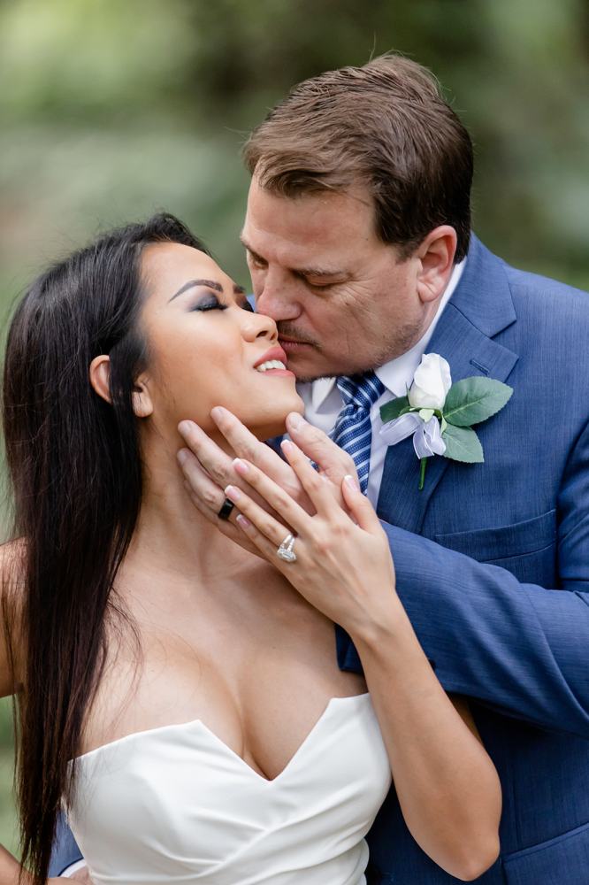 Couple embracing closely, woman smiling, man in a blue suit with flower boutonniere.
