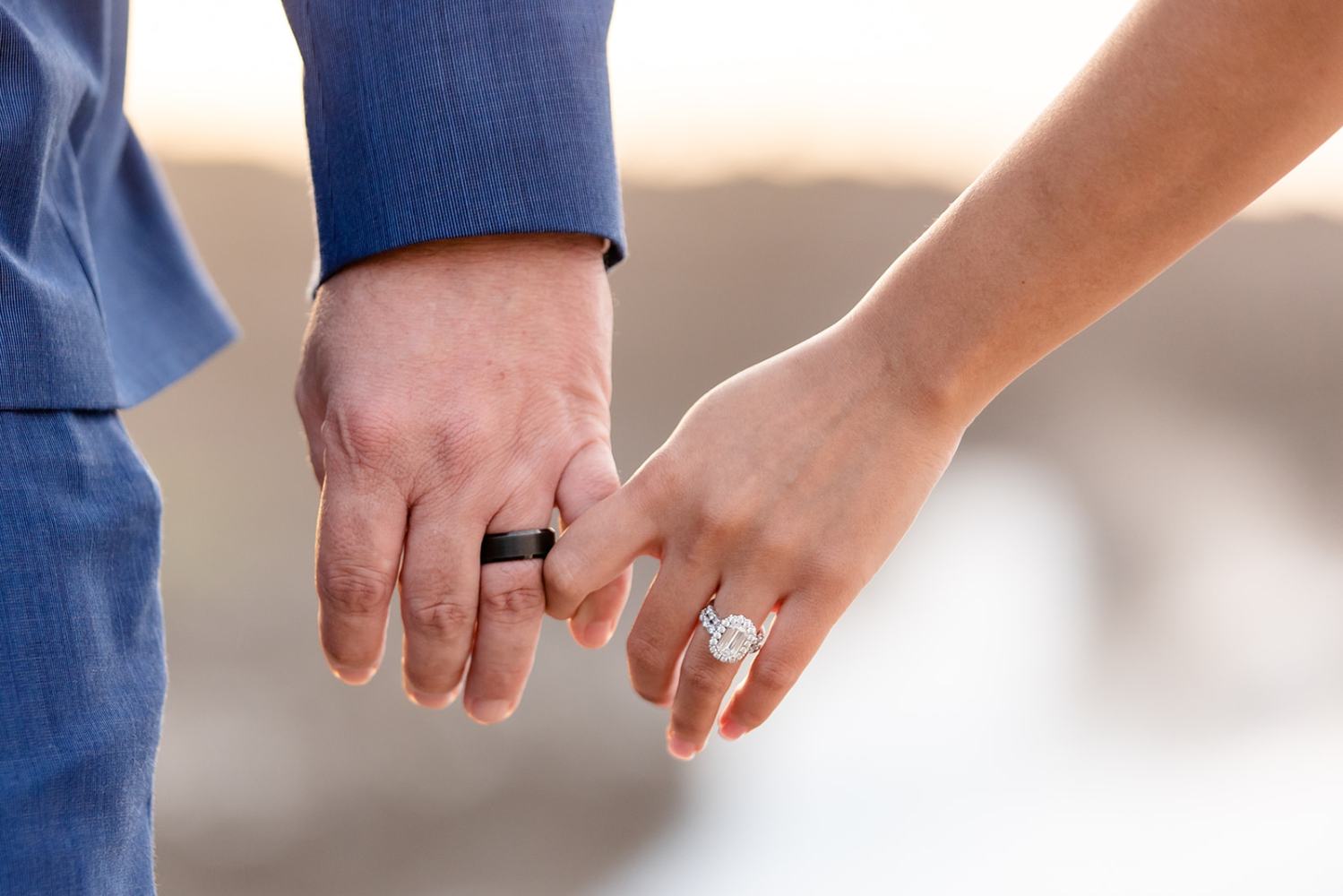 Close-up of two hands clasped; one with a wedding ring and the other with an engagement ring.