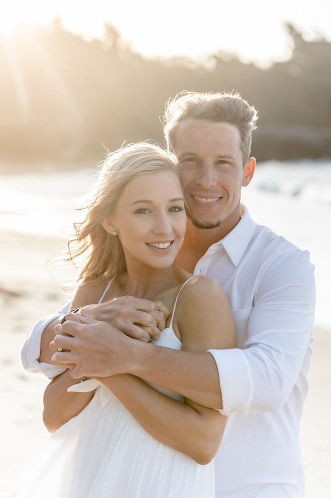 Couple in white clothes embracing on a sunlit beach.