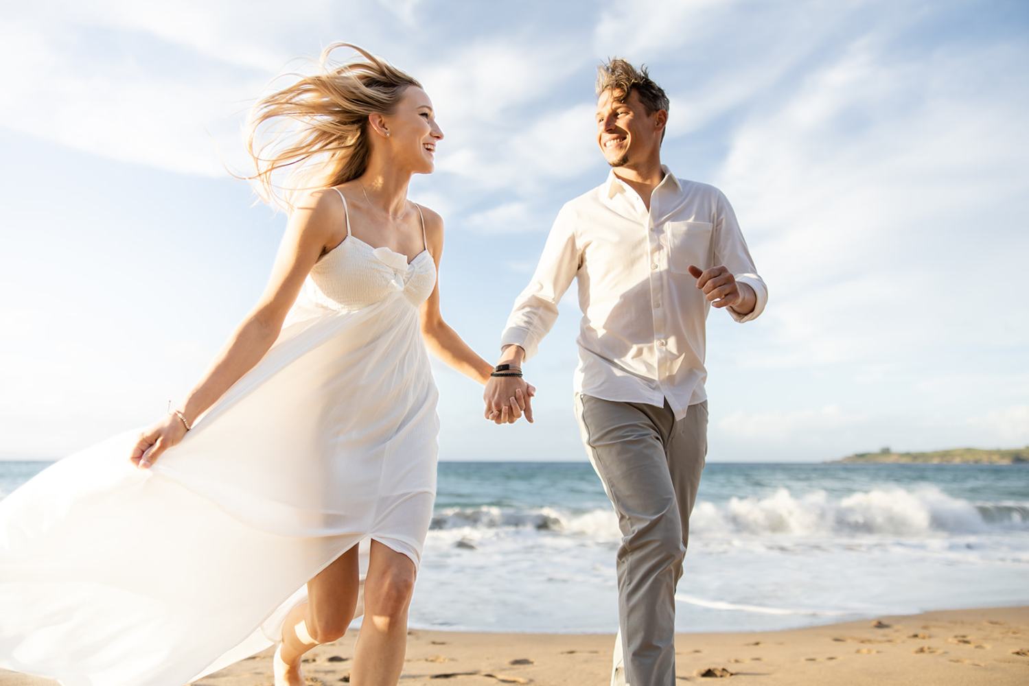Couple joyfully running hand in hand on a sunny beach.