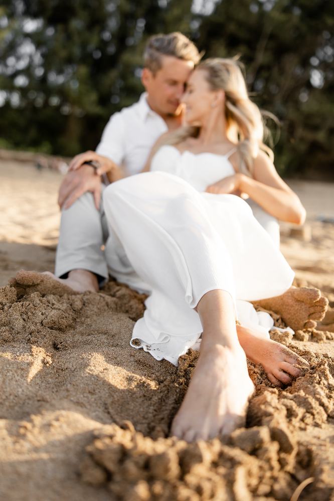 Couple sitting together on the beach with sandy feet, embracing intimately.