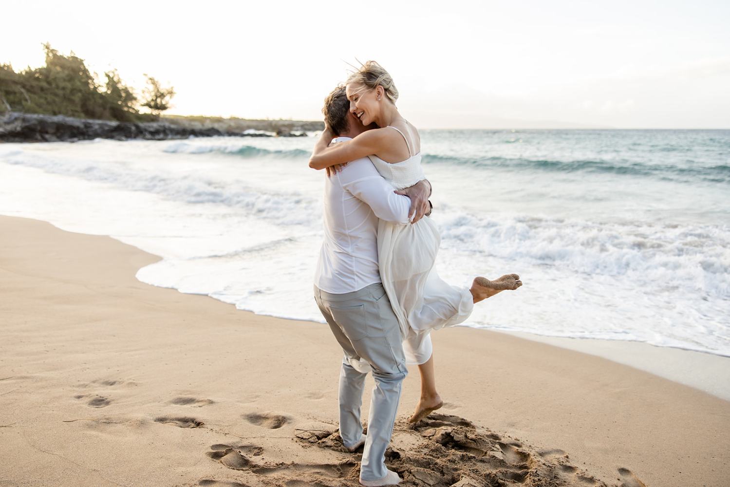 Couple embracing on a sandy beach with waves in the background.