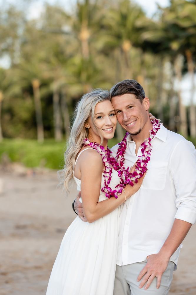 Couple with flower leis smiling and embracing on a beach.