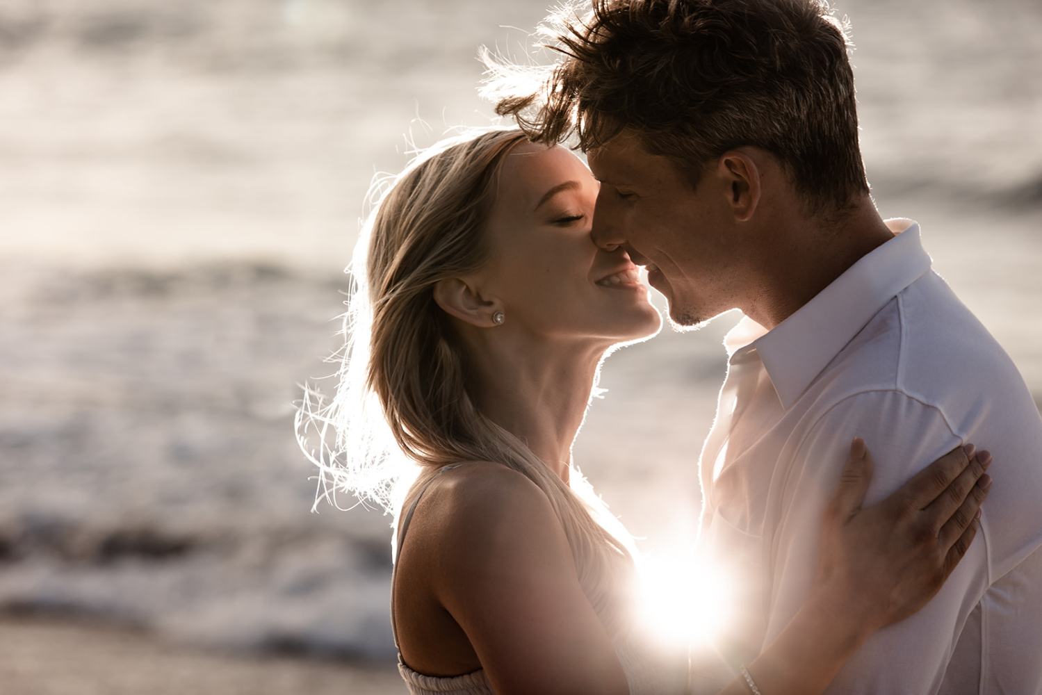 A couple embracing and smiling at sunset on a beach.