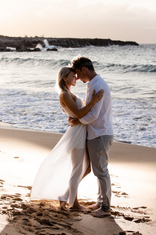 Couple embracing on a beach at sunset, waves in background.