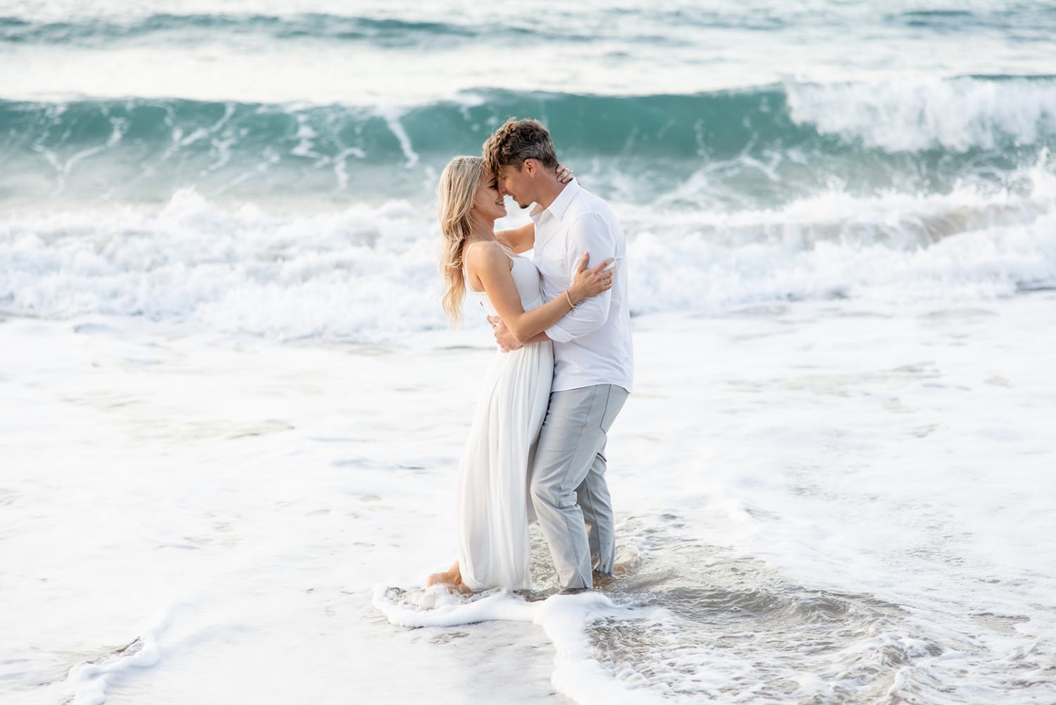 Couple embracing on a beach with waves in the background.