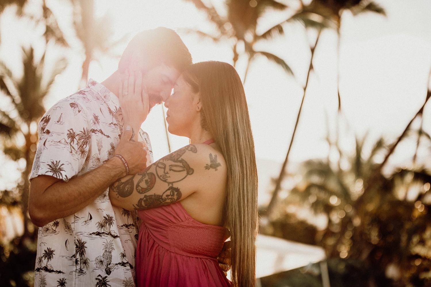 Couple embracing under palm trees with warm sunlight in the background.