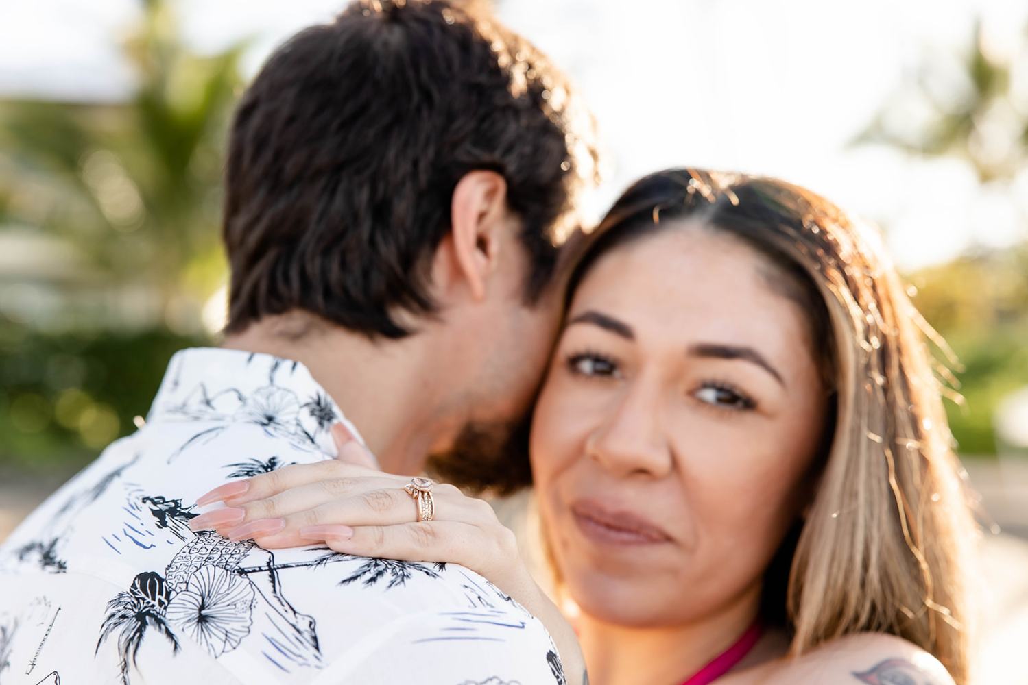 Woman smiling with hand on man's shoulder, showing engagement ring.