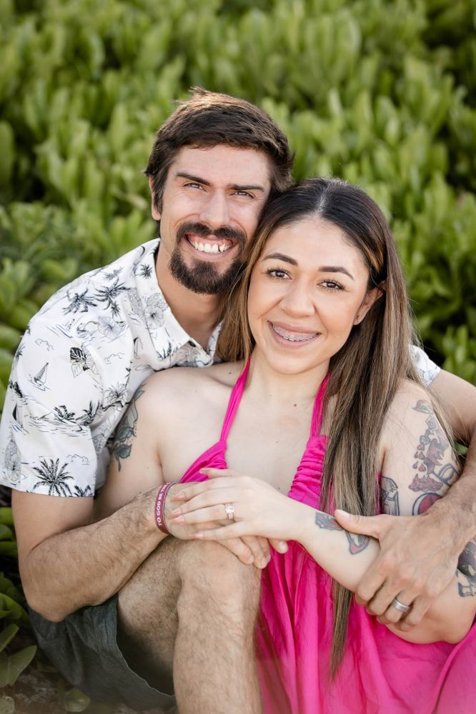 Smiling couple sitting closely in front of green plants.